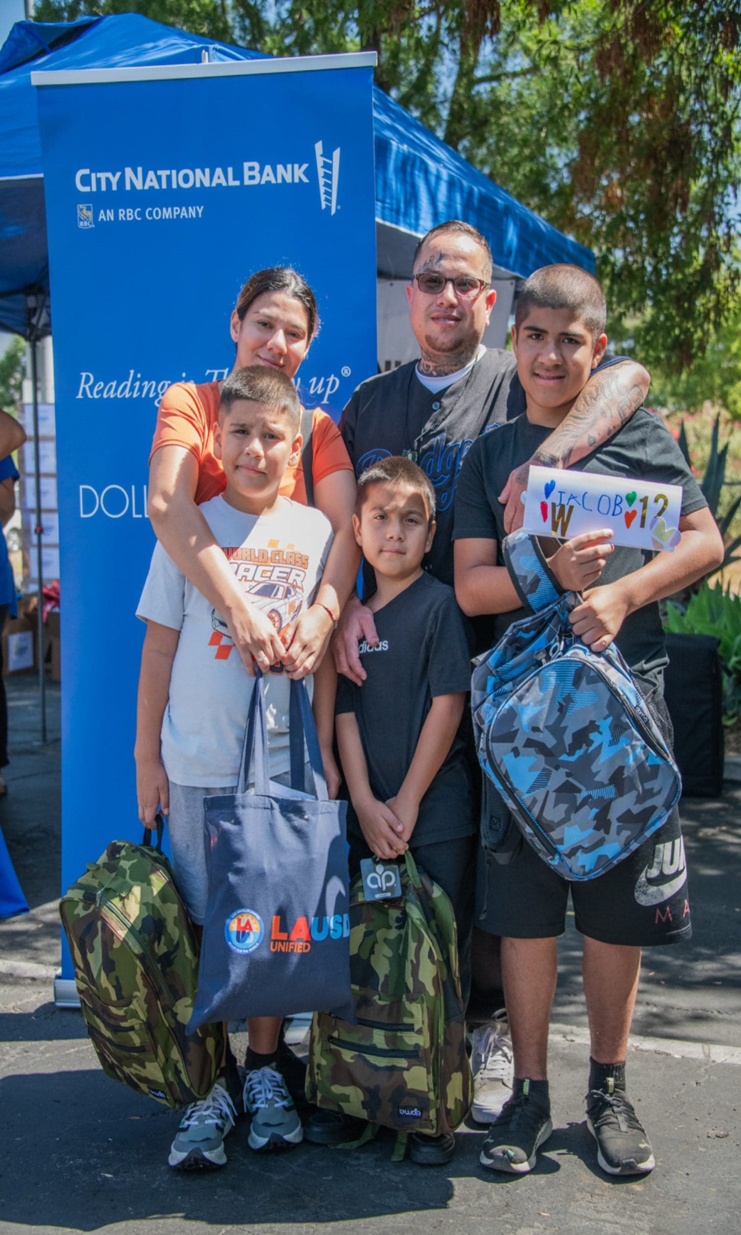 LA Family Housing participants. A family standing together. Two parents and three boys holding backpacks.