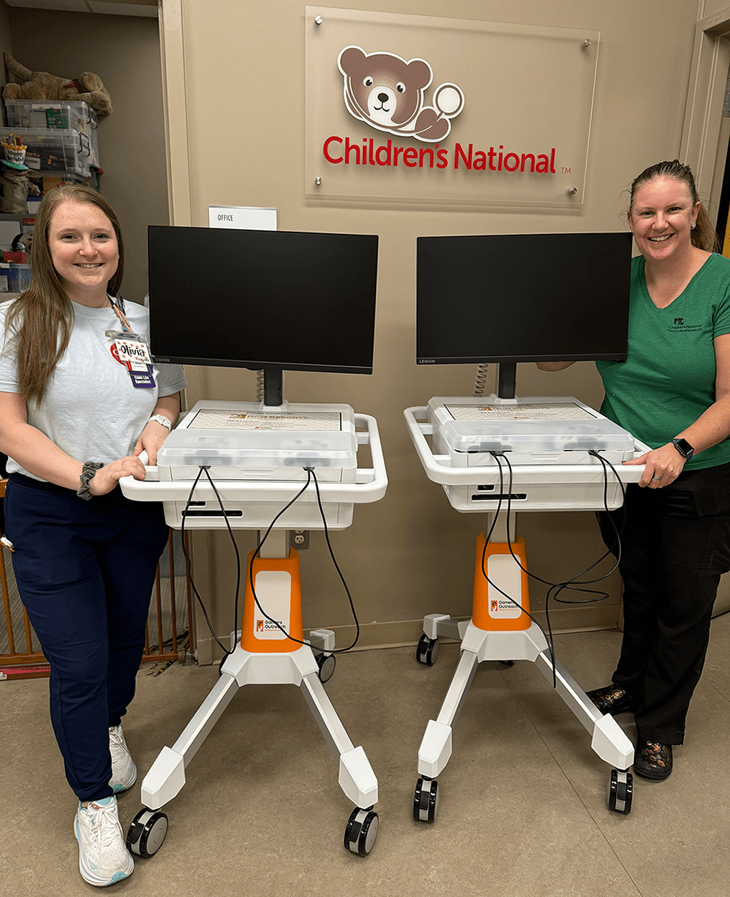 Photo of two nurses taking a photo by 2 Gamers Outreach Karts. GO Karts are a mobile gaming kiosk designed for hospitals, so kids have access to video games.