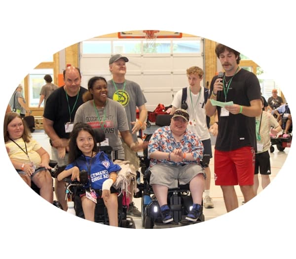 Group of campers standing and sitting in wheelchairs, happy and listening to an announcement by a staffer.