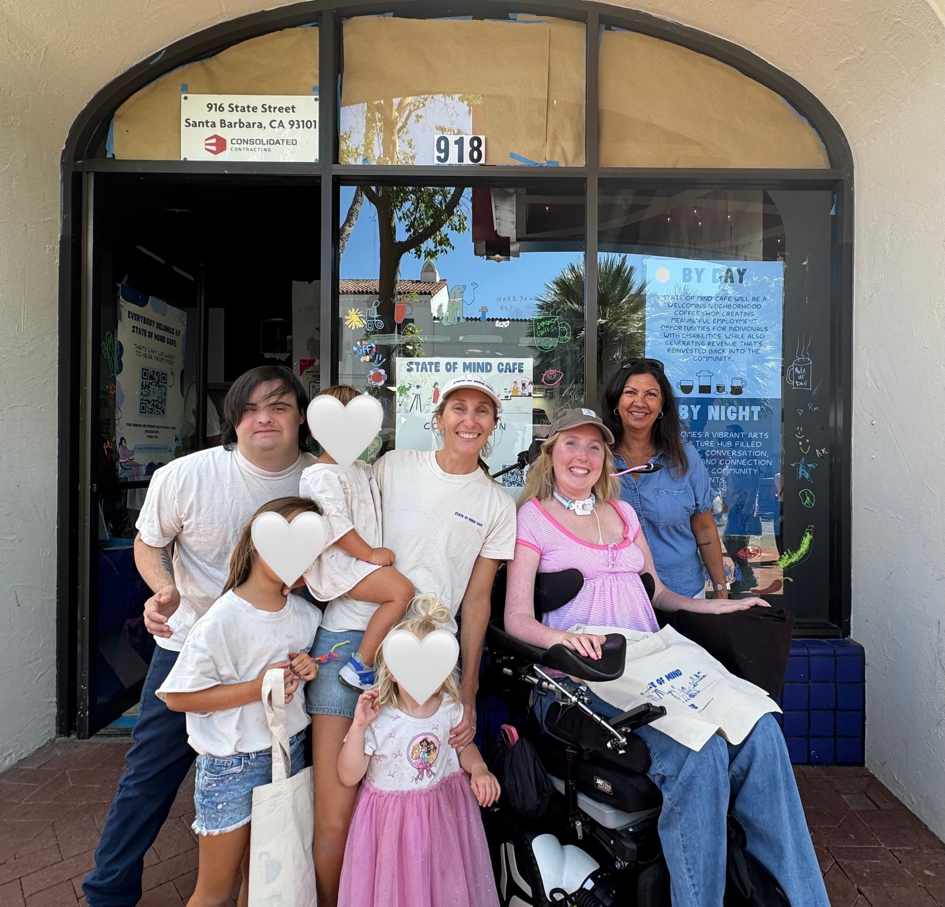 A group of people standing and smiling in front of the storefront at 918 State Street. There are four adults, one using a wheelchair, and three children.